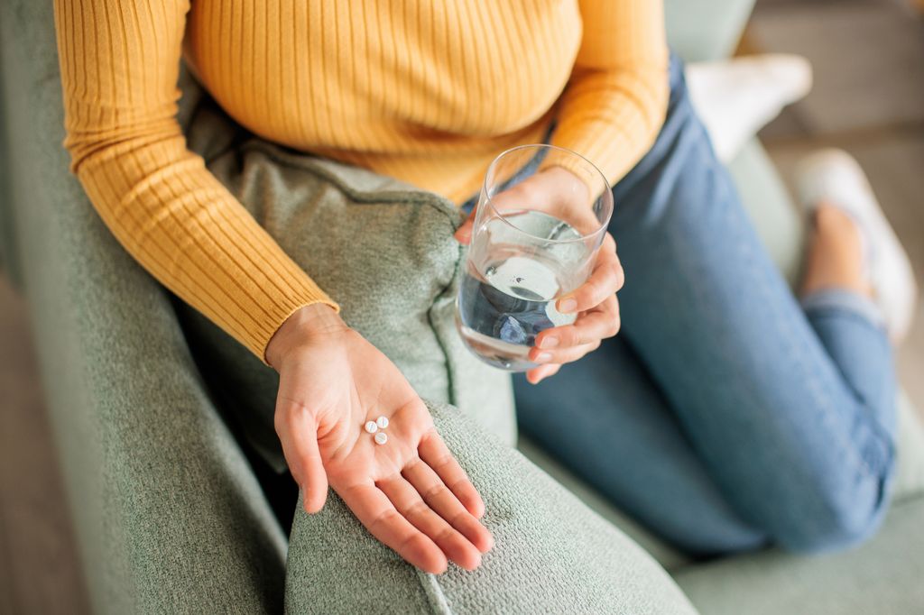Unrecognizable woman holds a glass of water in one hand and pills in the other, ready to take her medication.