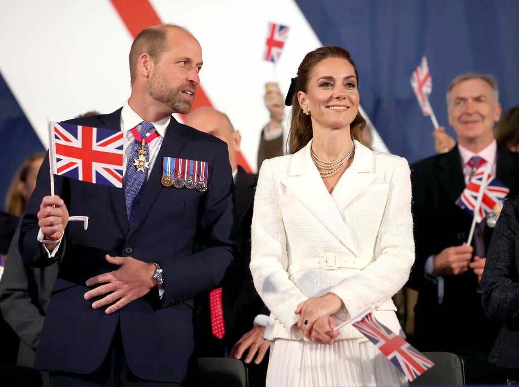 William and Kate smiling and waving flags in royal box at VE Day concert