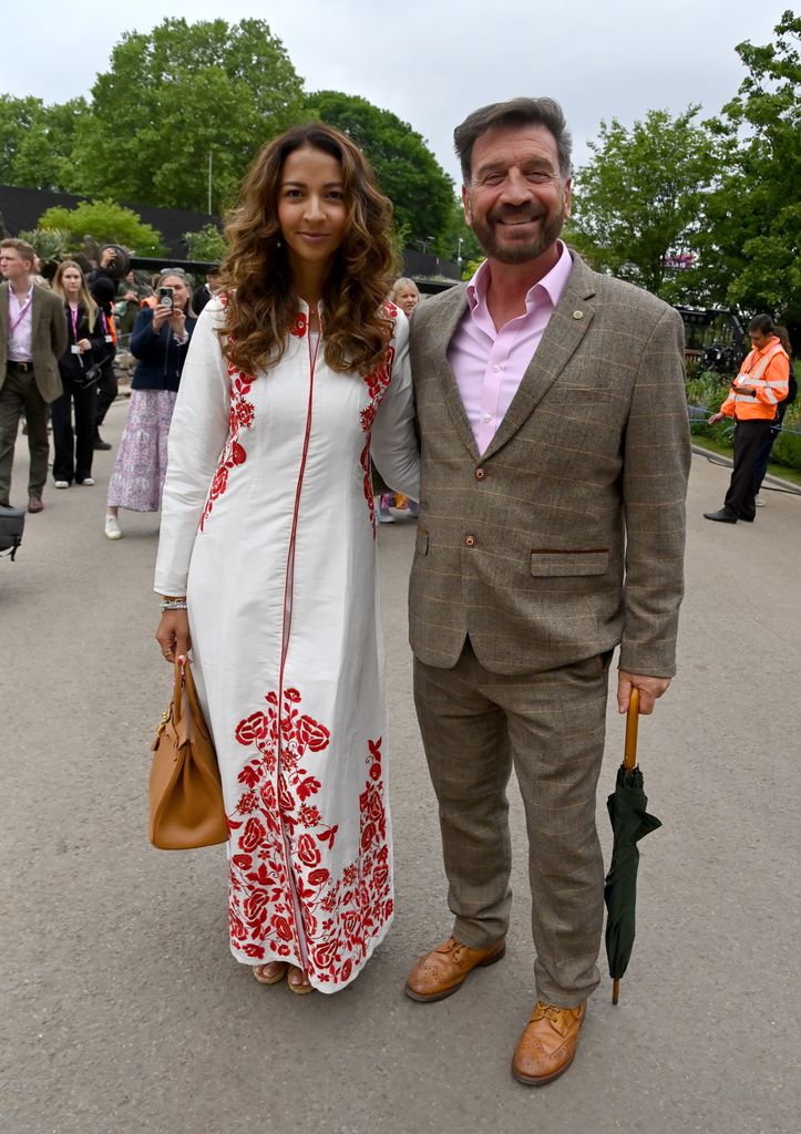 Katie Dadzie in a white and red embroidered maxi dress stands next to Nick Knowles in a tweed suit with a pink shirt.