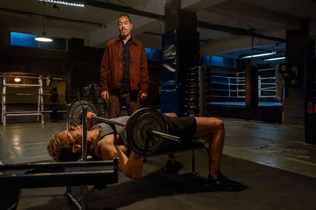man lifting weights in gym while second man watches