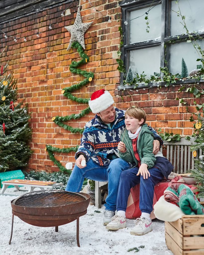 Jamie Oliver sitting on a bench with his son Buddy next to Christmas trees