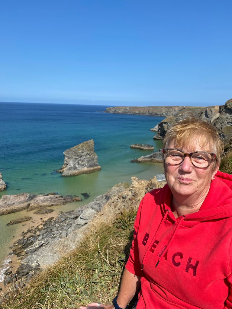 Woman smiling in a red hoodie on a cliff top