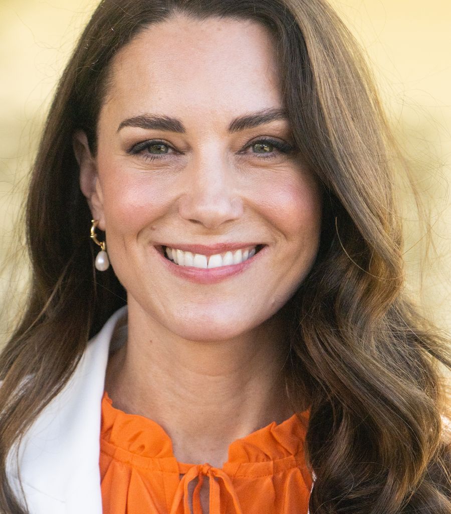 Kate Middleton, the Princess of Wales wears pearl earrings and a white blazer with orange blouse