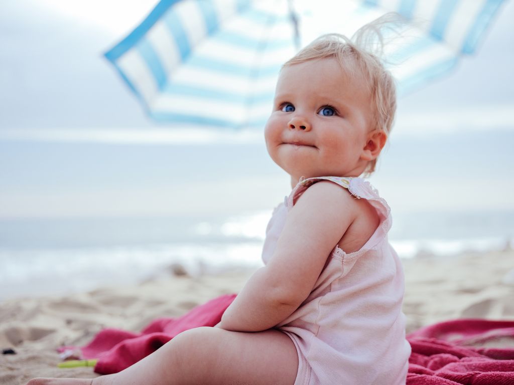 Happy little blondhaired toddler girl sitting at the beach.