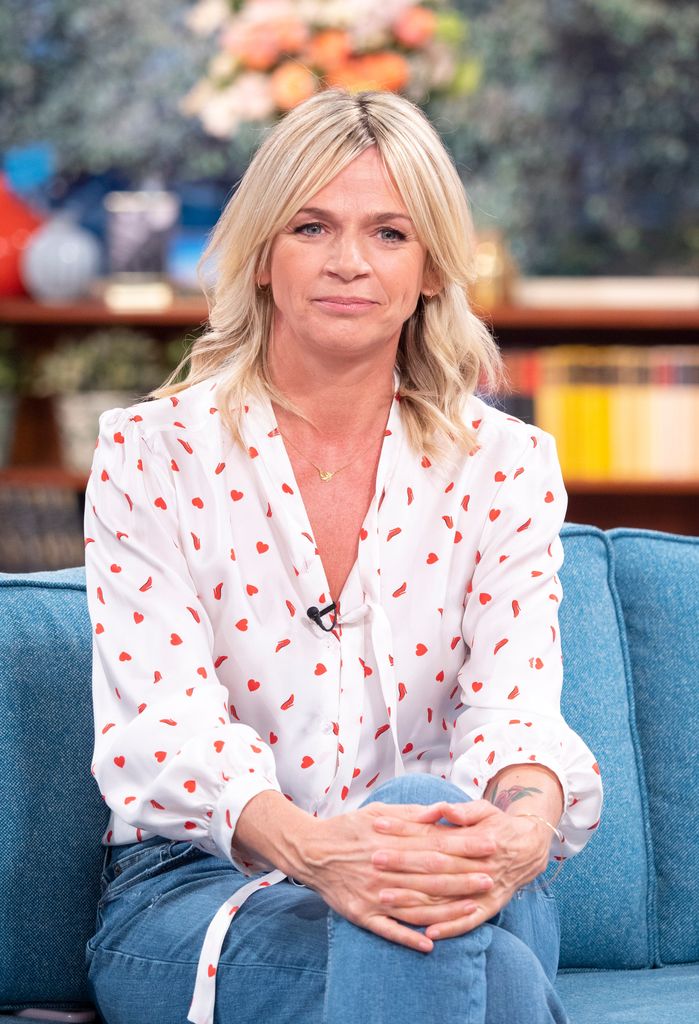 Zoe Ball in a white shirt and jeans sitting on a sofa