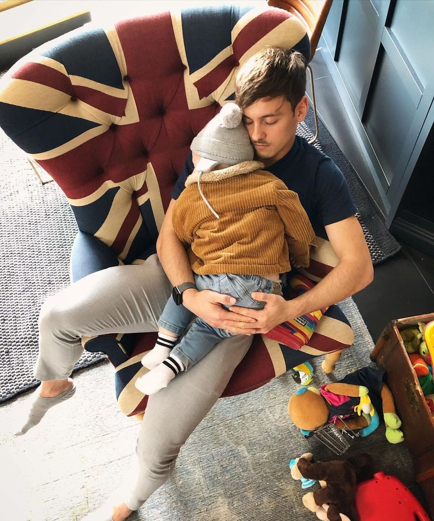 Tom Daley cradles his son Robbie whilst sitting on a Union Jack armchair