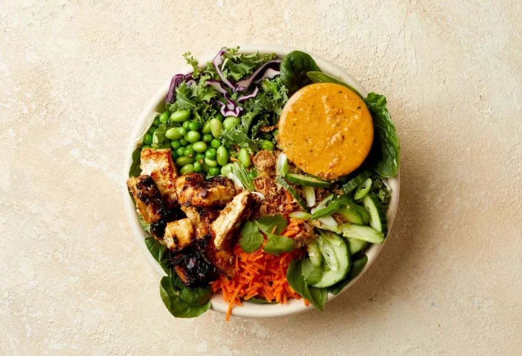 Atis salad bowl featuring grilled chicken leafy greens grated carrot and sauce