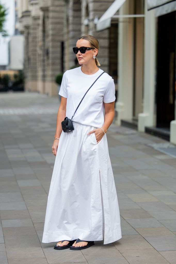 Tina Haase wears Arket white t-shirt, COS white maxi skirt, PolÃ¨ne black mini crossbody bag, Bobbies black leather flip flops, Chanel sunglasses during the Berlin Fashion Week SS25 