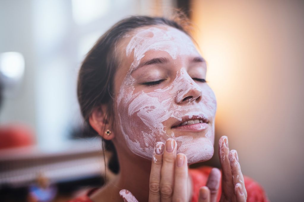 Woman using a beauty mask in front of a mirror.
