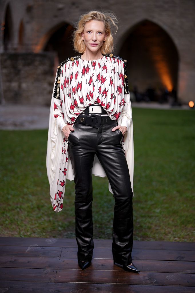 Cate Blanchett at the Louis Vuitton Cruise 2026 show wearing black leather trousers and a caped top in white with a red lightning bolt print