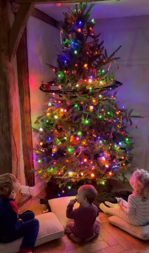 Three children sat in front on a Christmas tree all lit up