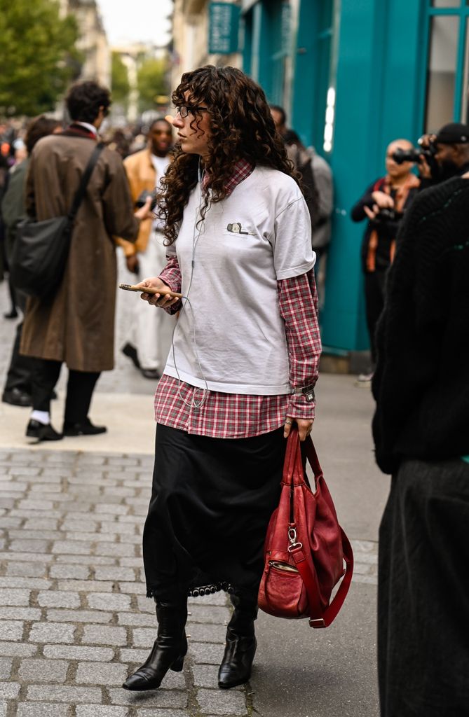 A guest is seen wearing a white shirt, red plaid shirt, black skirt, black boots and red bag outside the Acne Studios show during the Womenswear Spring Summer 2026