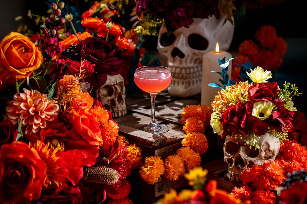 Halloween cocktail surround by orange flowers and skulls