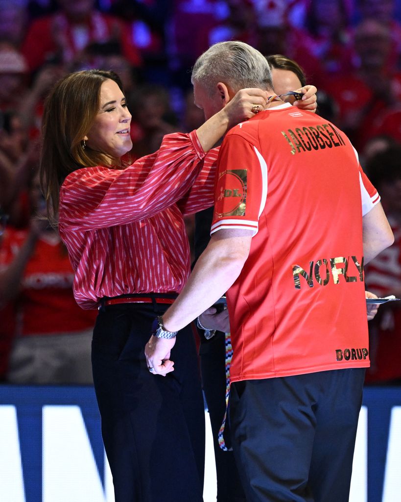 Queen Mary in red shirt putting medal around coach's neck