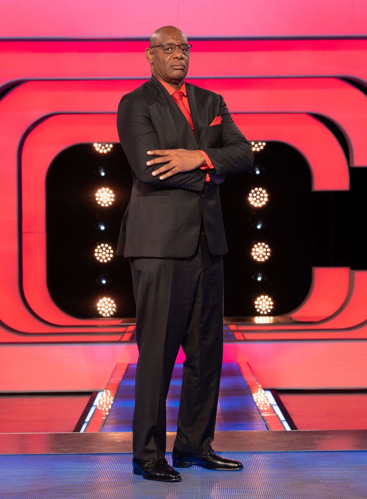 Man in black suit standing in tv studio with arms folded