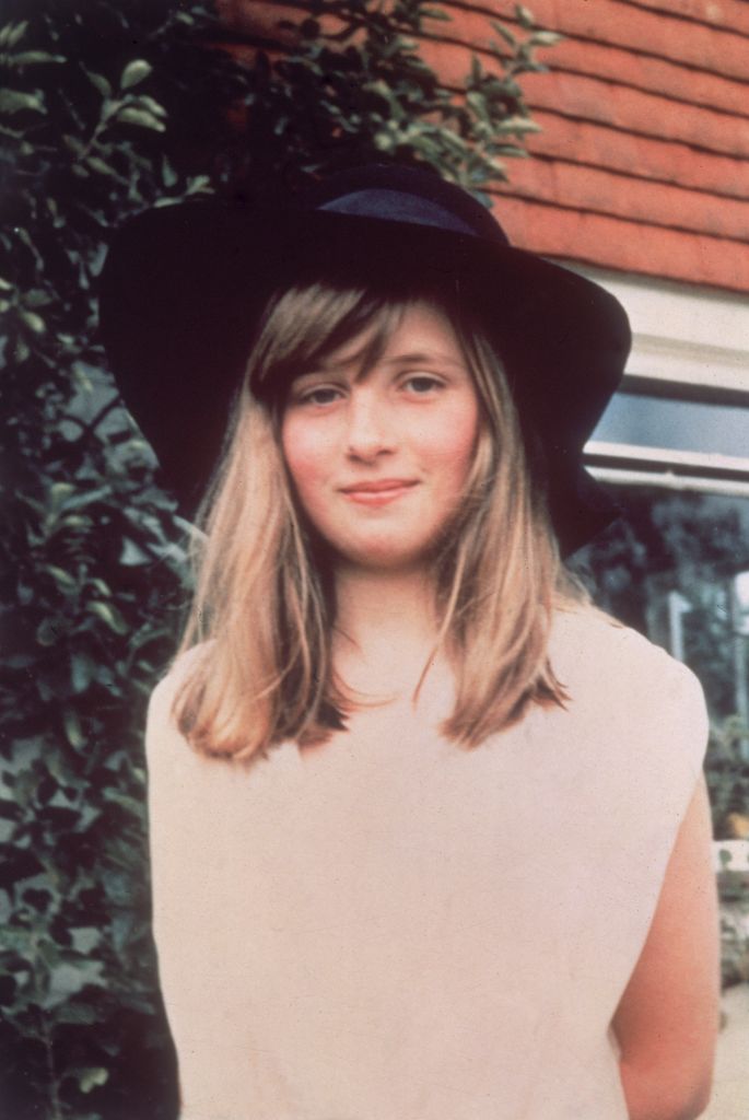A young Princess Diana in a cream dress and black hat