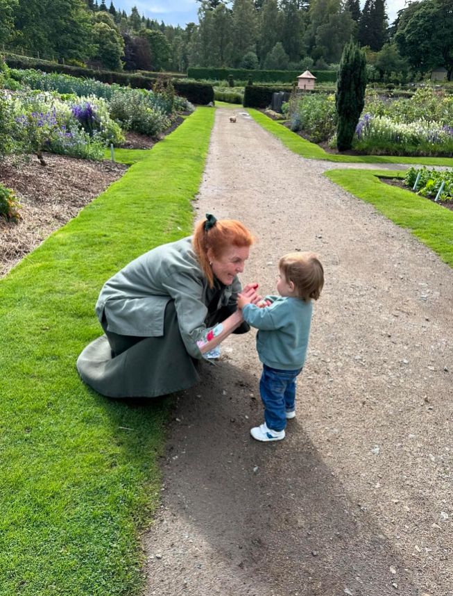 Sarah Ferguson crouching down in a garden to talk to a small boy