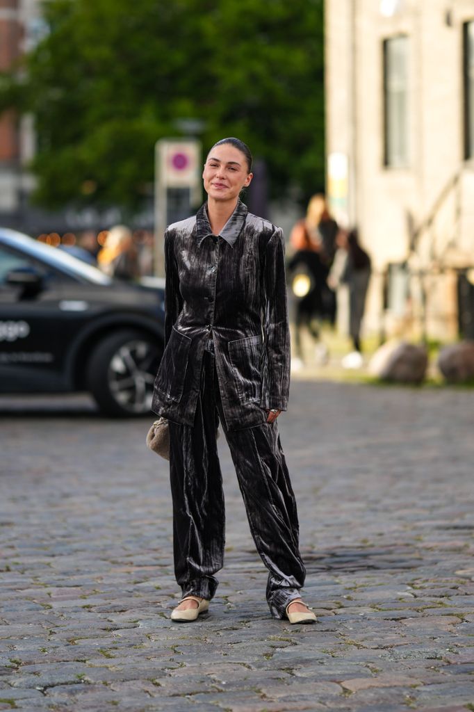 Sophia Roe wears a dark gray velvet belted blazer jacket, matching dark gray velvet large pants, a beige sheep fur handbag, beige matte leather ballerinas , outside Ganni, during the Copenhagen Fashion Week Spring/Summer 2024