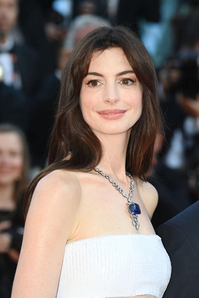 Anne Hathaway with her hair loose wearing a large sapphire necklace 