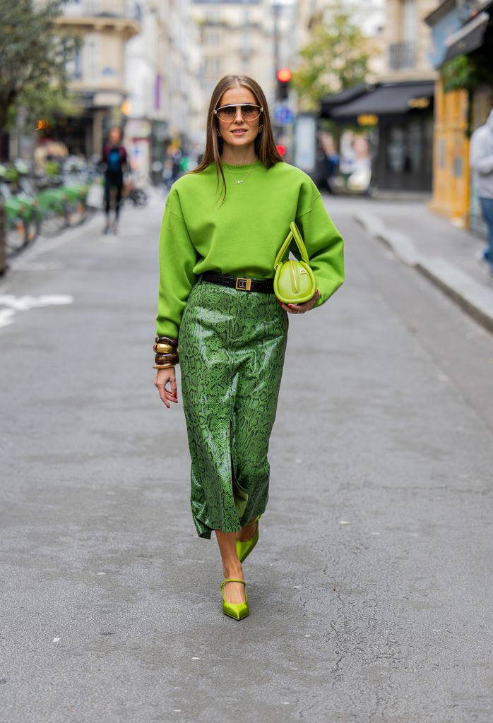 Nina Sandbech wears a green jumper, darker green snake print midi skirt, green satin heels and carries a green bag. 