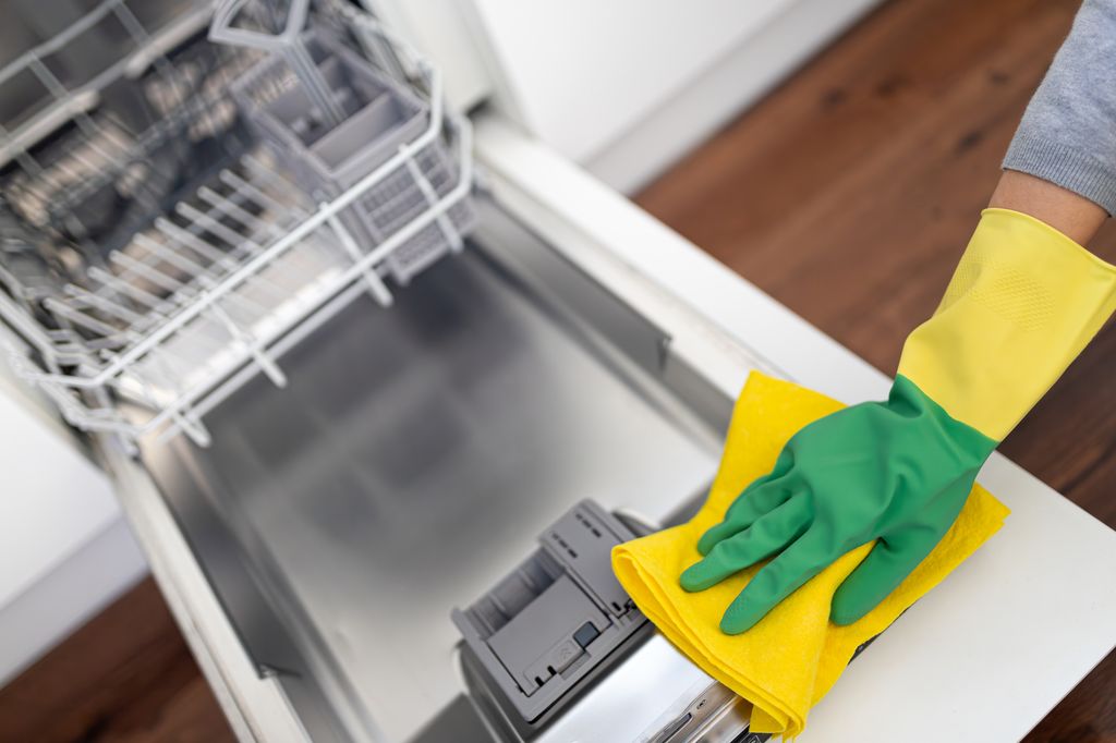 High angle view of unrecognizable person hand wearing gloves cleaning dishwasher with yellow cleaning cloth.