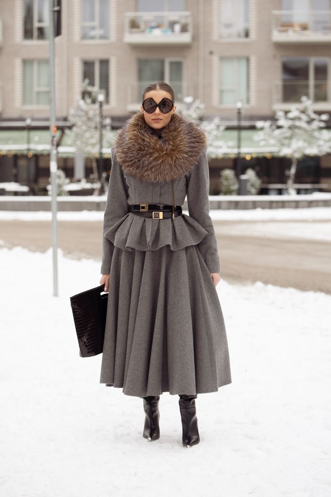 Nina Sandbech wears grey skirt, grey long sleeve top with brown fur collar, double stacked black belts, black leather bag, and Prada sunglasses  outside the Forza Collective show