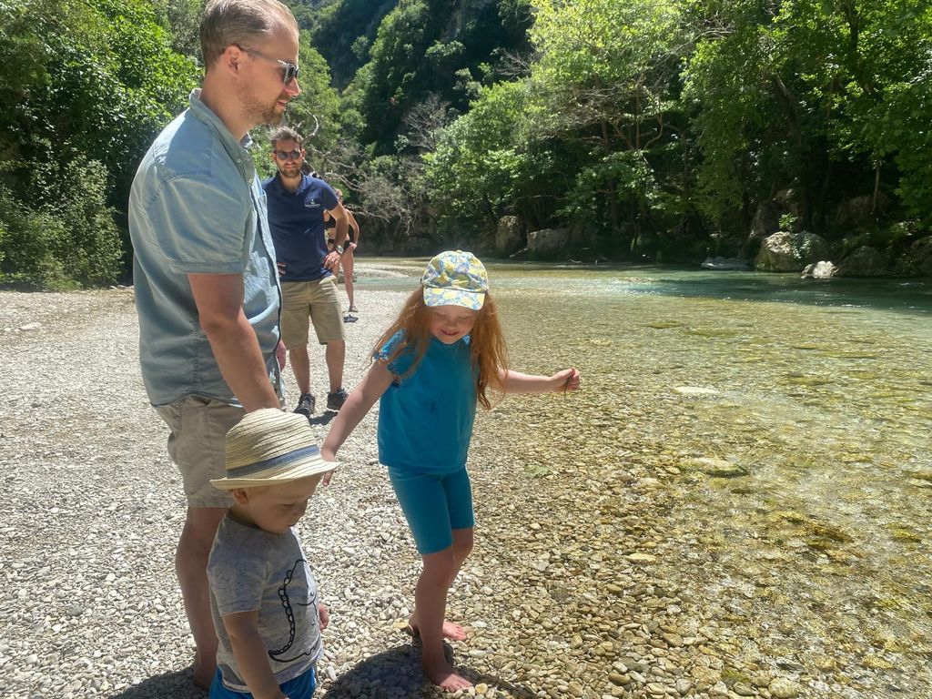 Man holding hands with two young children next to a pebbled spring with trees in the background