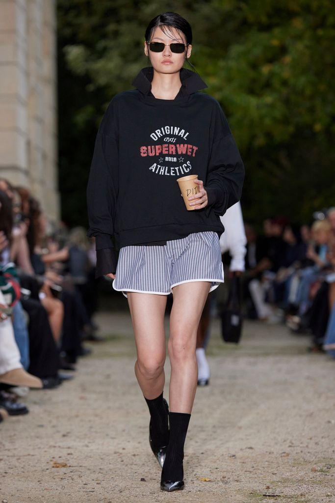 A model pairs blue and white striped shorts with a hoodie (and a coffee) at Didu SS24
