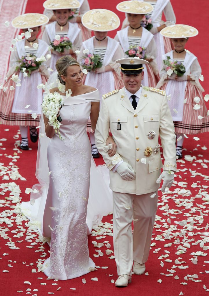 Princess Charlene with her hand through Prince Albert's arm as they're showered with petals following their wedding