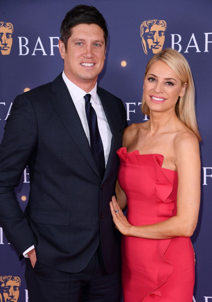 Vernon Kay in suit standing with Tess Daly in red dress