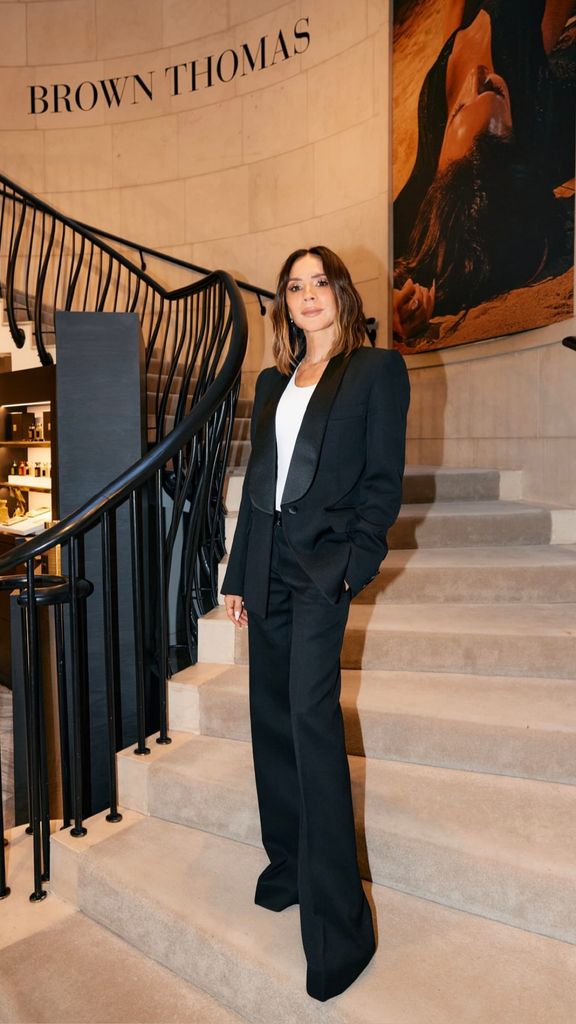 Victoria Beckham in a black suit standing on steps