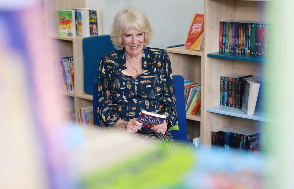 Queen Camilla in a primary school library with a copy of Horrid Henry