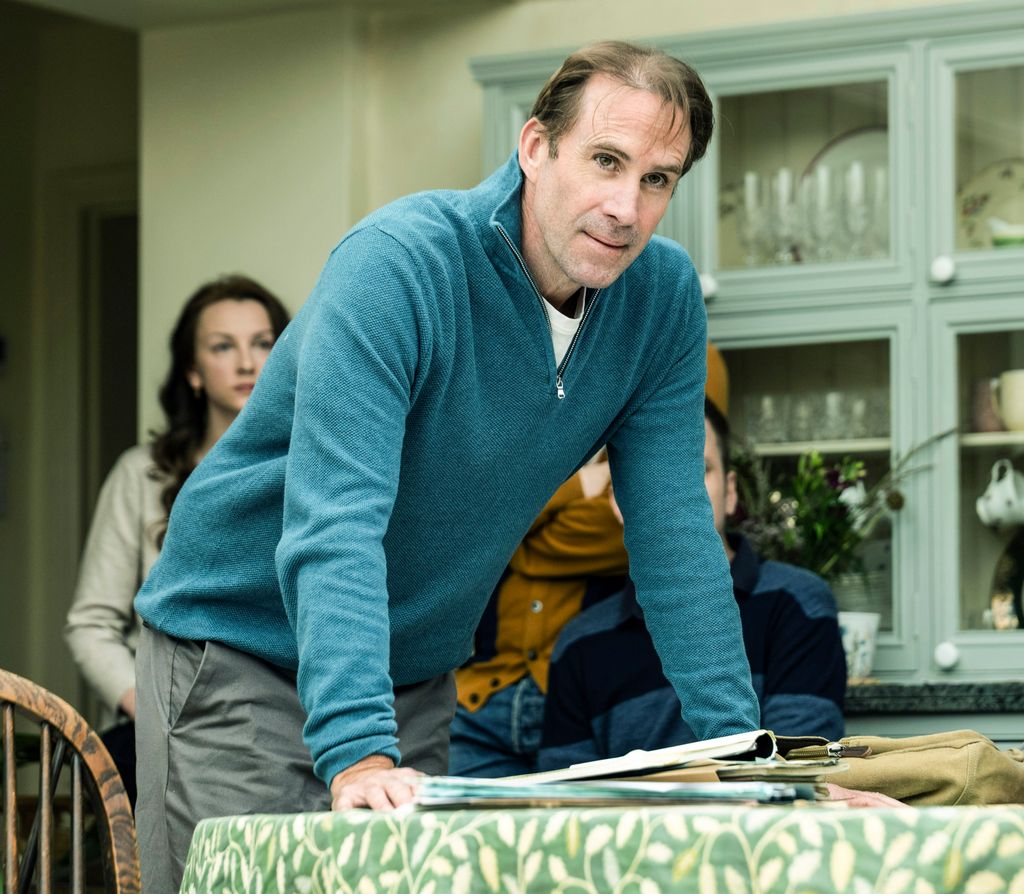 A photo of a man wearing a blue jumper in a kitchen