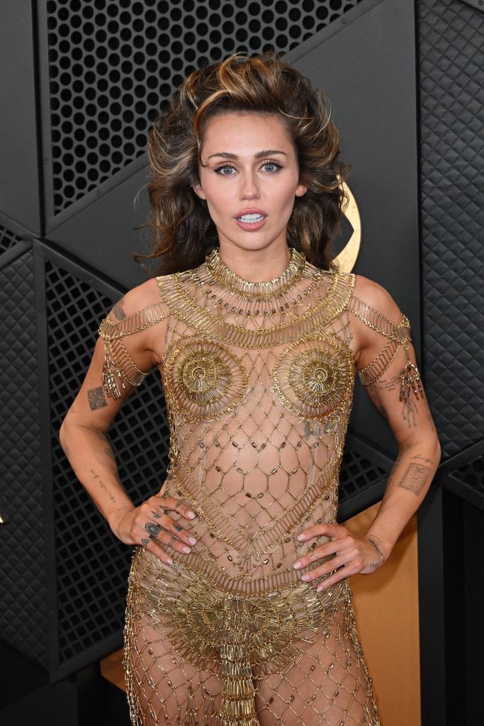 Miley Cyrus wearing a gold mesh dress at teh Grammys displaying her tattoos 