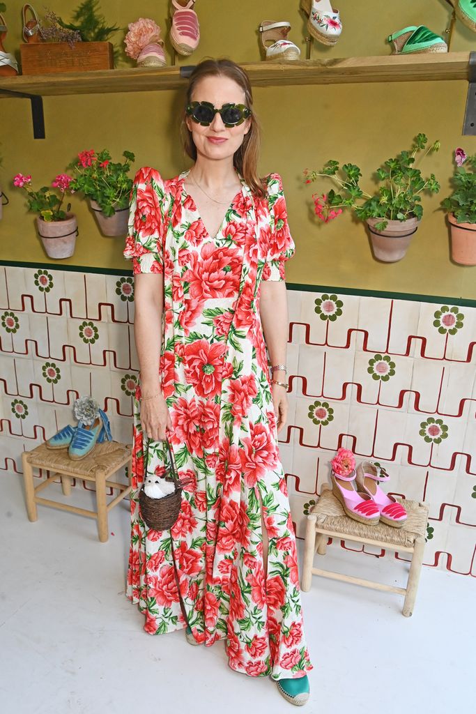 Kelly Eastwood wearing a red and white floral dress, green espadrilles and sunglasses shaped like leaves, holding a Lulu Guinness basket bag with a stuffed bird at Chelsea Flower Show 2025.