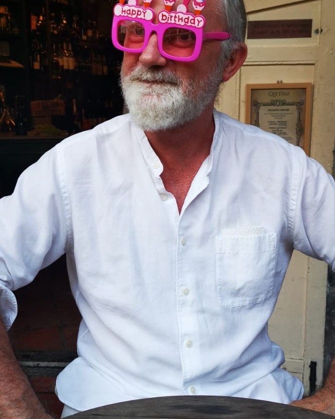 man sat at table wearing pink birthday glasses 