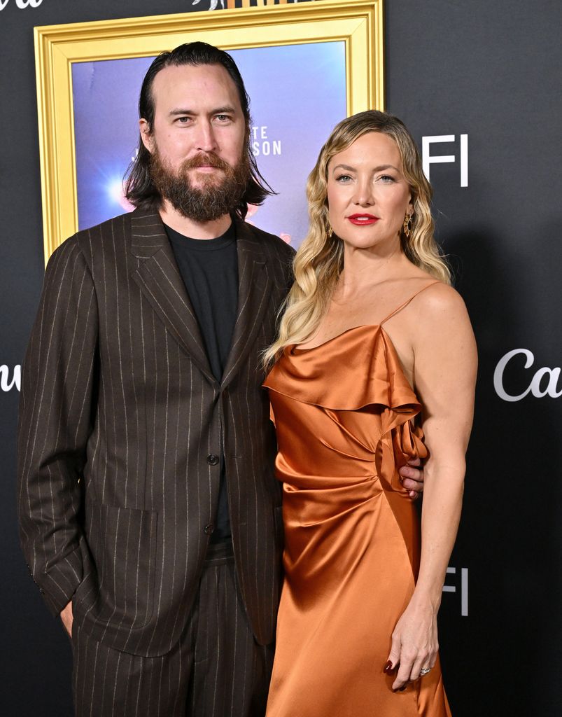 Danny Fujikawa in stripe suit and Kate Hudson in orange dress at the premiere of Song Sung Blue 