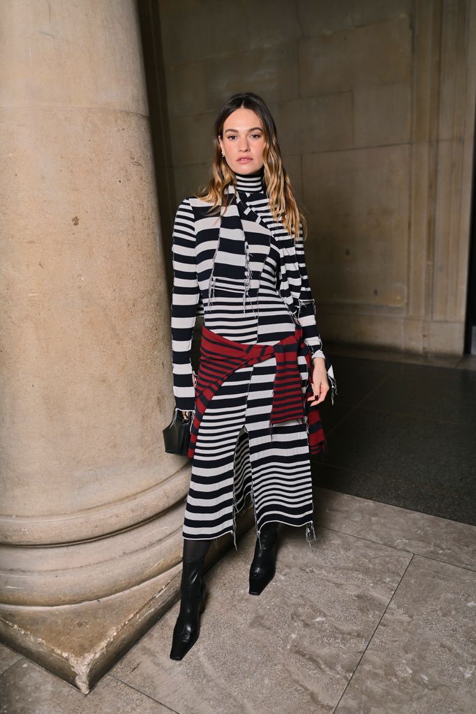 Lily James est une illusion d'optique dans un look moulant inattendu 1 Lily James porte une robe rayée avec des bottes noires et un pull rouge noué autour de la taille.