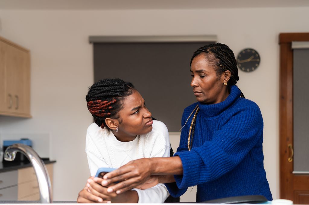 Mother taking away a smartphone from her teenage daughter while arguing in a kitchen
