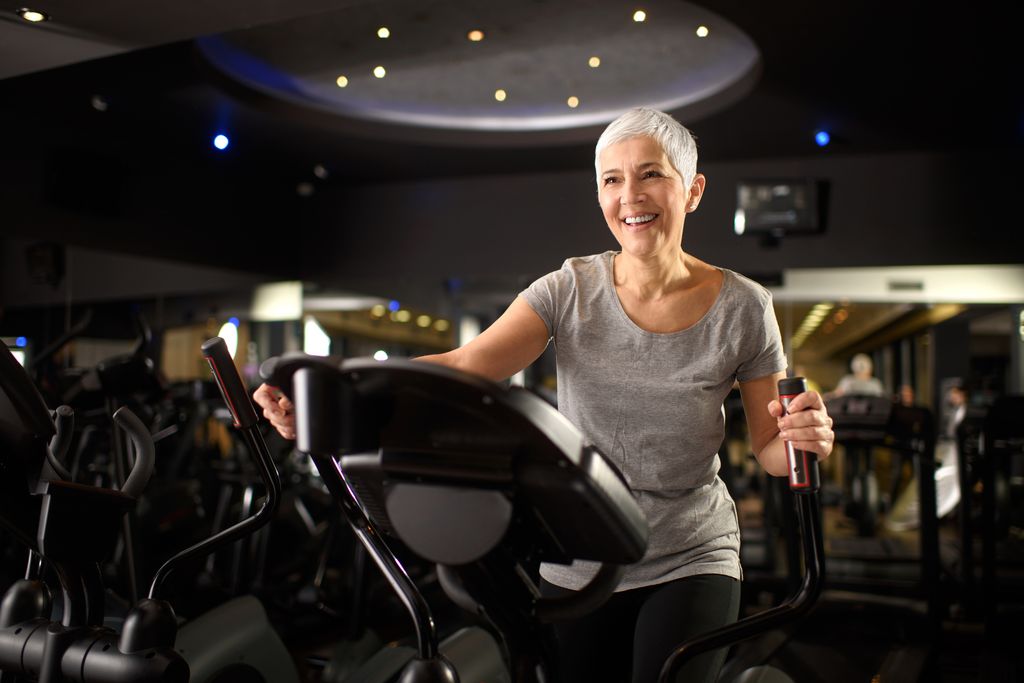 Active senior female exercising on the cross trainer machine in a health club.