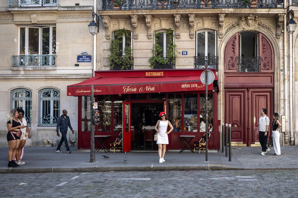 A woman wearing a red beret poses for photographs next to the restaurant "Terra Nera", one of the many iconic Paris locations to feature in the hit Netflix series "Emily in Paris", in Paris, on August 27, 2024. The large wooden doors to a understated building on Place de l'Estrapade, the bright red awning of a restaurant terrace on Rue des Fosses Saint-Jacques in Paris' 5th arrondissement (district), or the office entrance next to a an art gallery on Place Valois: Like pilgrims, fans and tourists flock to take selfies, sometimes sporting an iconinc red beret, in front of these new Paris "landmarks" made famous by the global hit Netflix streaming service series "Emily in Paris" which releases the second part of its fourth season September 12. (Photo by Olympia DE MAISMONT / AFP) (Photo by OLYMPIA DE MAISMONT/AFP via Getty Images)