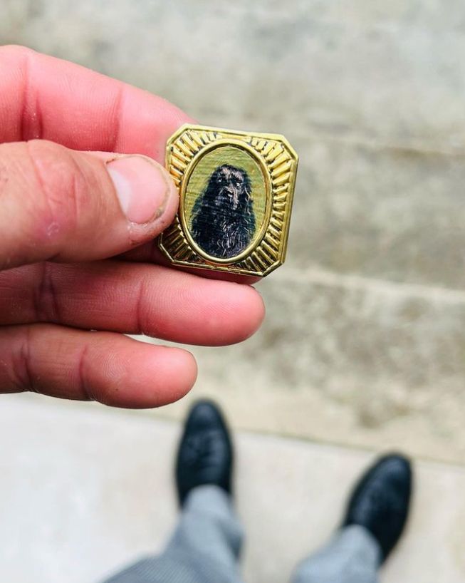 A gold cufflink with the image of a black dog