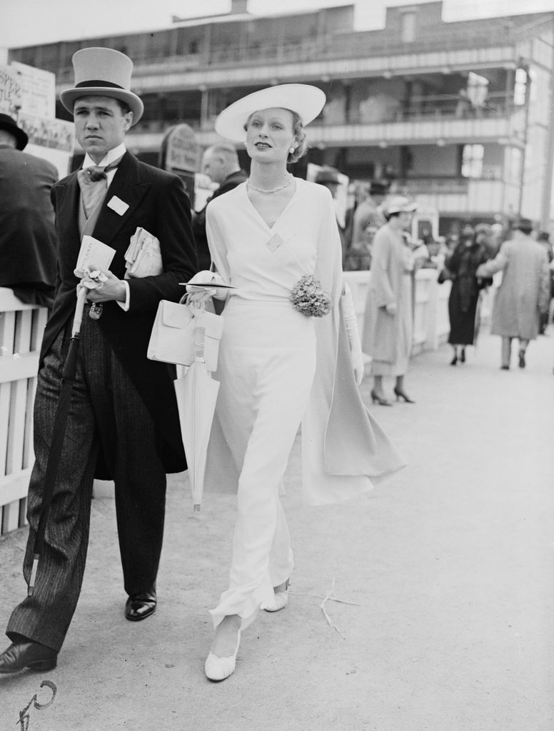 UNITED KINGDOM - NOVEMBER 07:  Couple at Royal Ascot, 1935. A photograph of a couple walking past racegoers at the Royal Hunt Cup horse-race, taken by Edward Malindine for the Daily Herald newspaper on 19 June, 1935. The woman appears in an elegant white ensemble, whilst her partner wears top hat and tails - traditional dress by the 1930s. The racecourse at Royal Ascot was founded by Queen Anne in 1711. As a racecourse favoured by British Royalty Ascot has become a highlight of the social season and is famous for its fashions, especially its hats. This photograph has been selected from the Daily Herald Archive, a collection of over three million photographs. The archive holds work of international, national and local importance by both staff and agency photographers.  (Photo by Daily Herald Archive/SSPL/Getty Images)