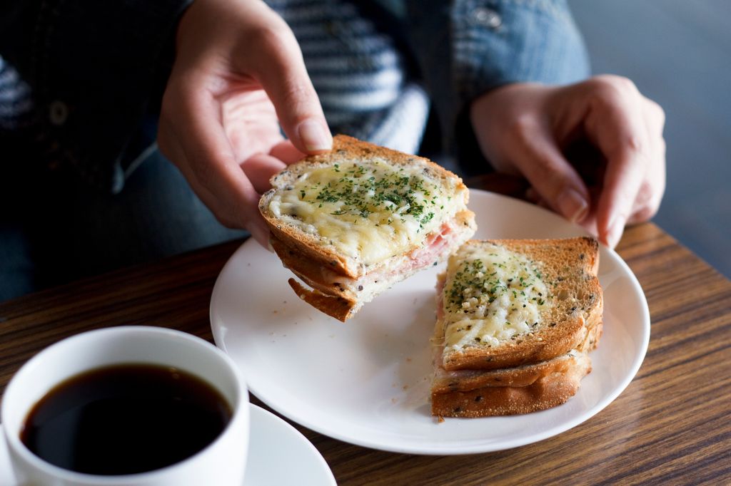 Close-up of hands of a woman holding croque-monsieur.