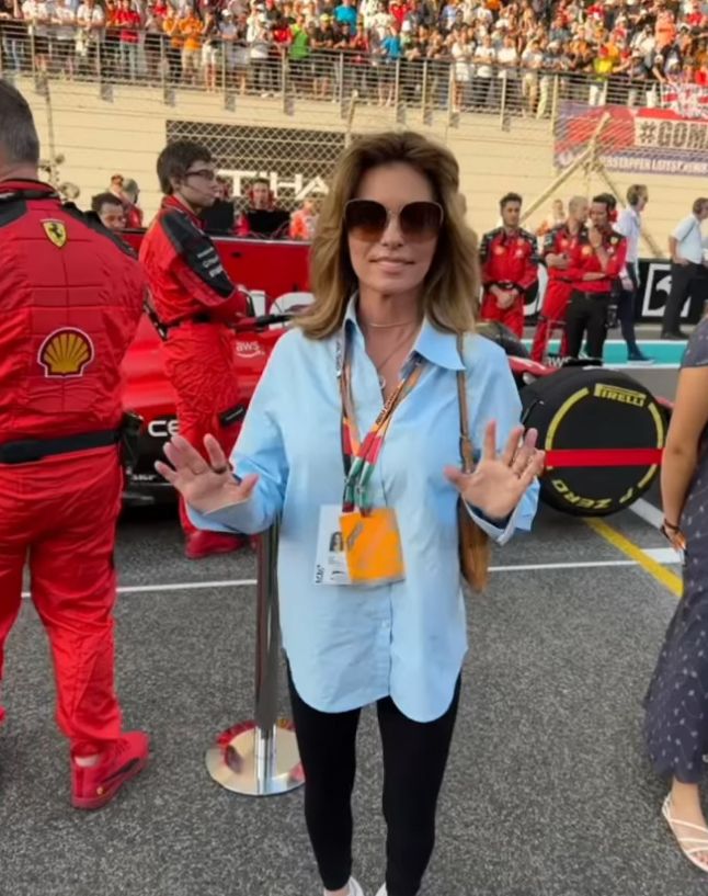 Shania Twain in a blue shirt and skintight pants in front of a Ferrari racing car