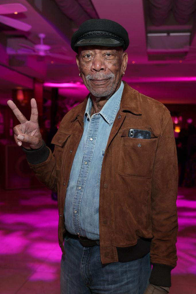 Morgan Freeman smiles and makes a peace sign with his right hand