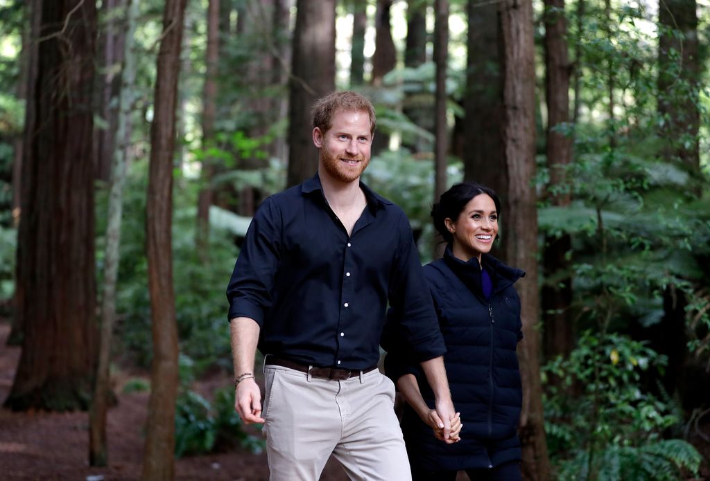 Meghan and Harry smiling as they walk in a forest
