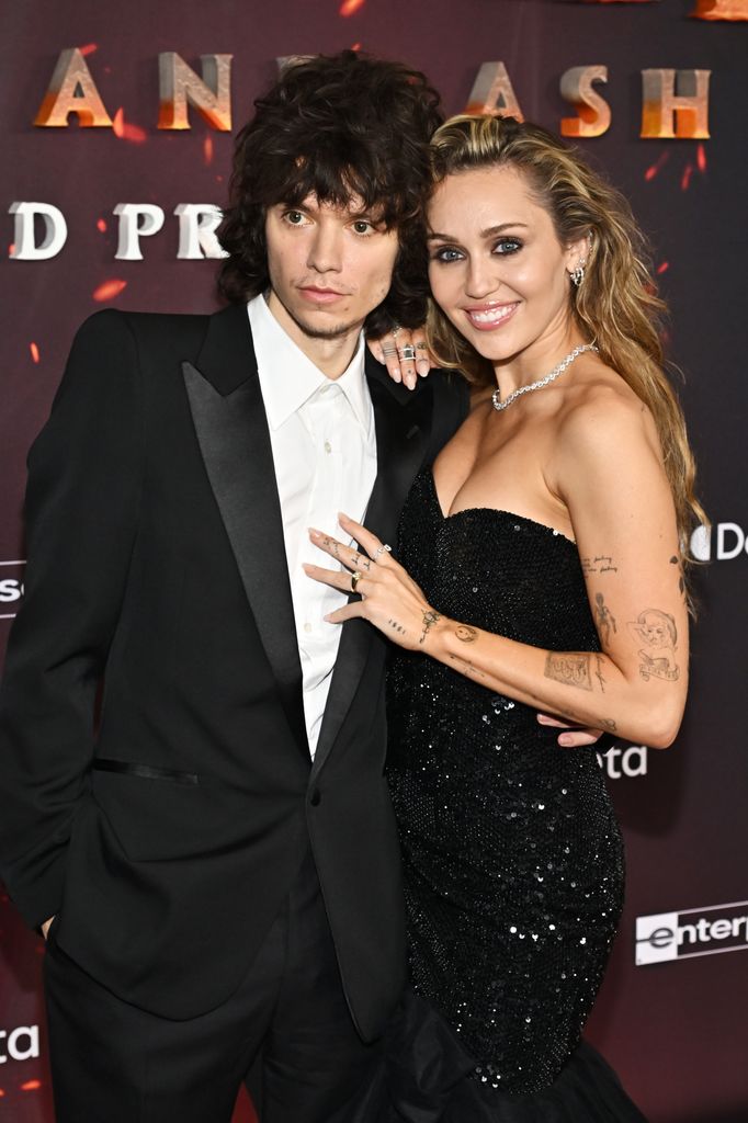 photo of miley cyrus in black dress with diamond ring on engagement finger with arms around boyfriend maxx morando