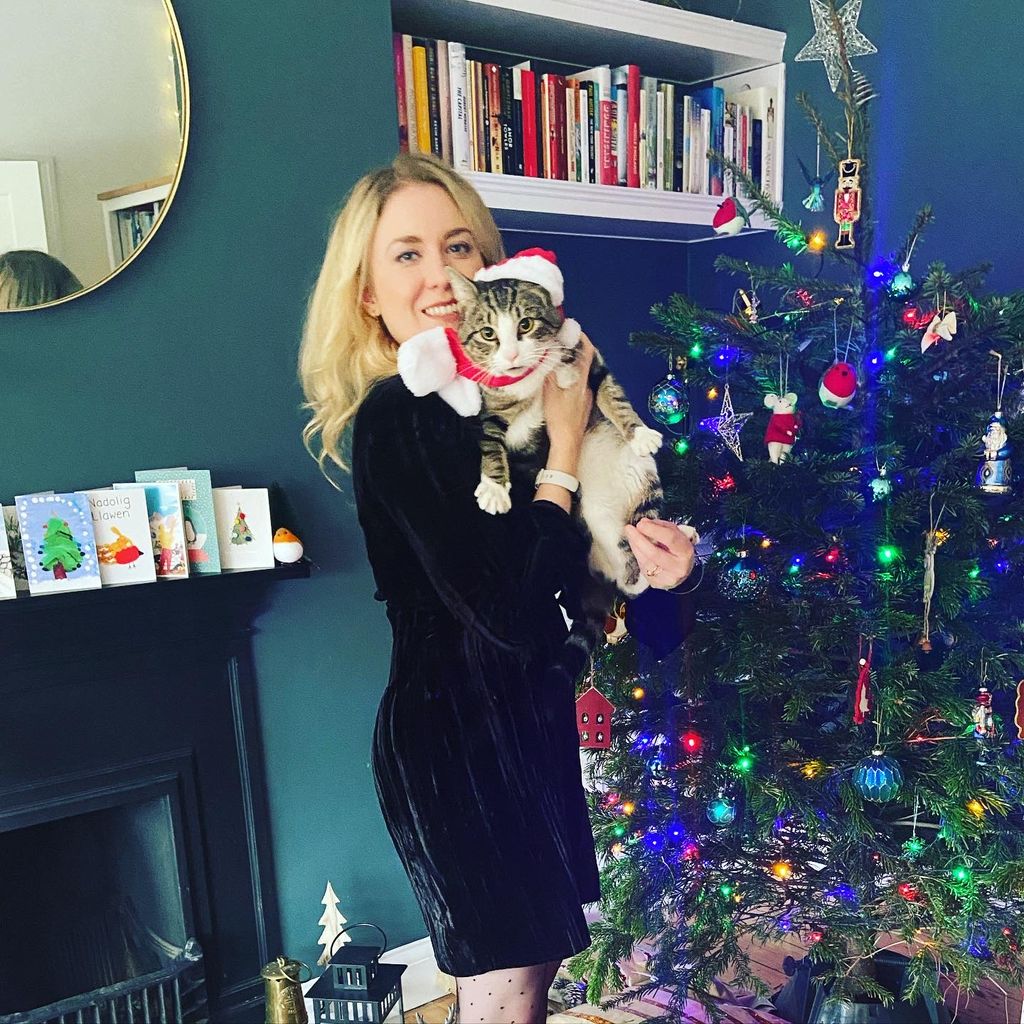 Woman holding her cat in front of a Christmas tree