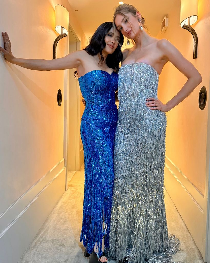 salma hayek and mathilde pinault posing in hallway wearing similar sequin gowns